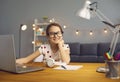 Online school training. Smart happy little girl in glasses smiles teaches a lecture using a laptop in the room. Royalty Free Stock Photo