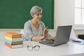 Online schooling. Senior teacher waving to students while communicating on laptop at class. Mature tutor giving lesson