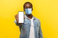 Online service, technology. Portrait of satisfied glad young man with medical mask standing holding out cellphone and smiling Royalty Free Stock Photo