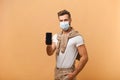 Online service, technology. Portrait of satisfied glad young man with medical mask standing holding out cellphone and Royalty Free Stock Photo