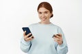 Online shopping. Beautiful young woman shops on website, app, paying with mobile phone and credit card, smiling Royalty Free Stock Photo