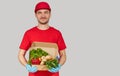 Online shopping concept. Male courier in red uniform and gloves with a grocery box with fresh fruits and vegetables. Royalty Free Stock Photo