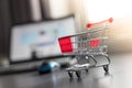 Concept of online shopping: Little shopping cart and a laptop in the blurry background Royalty Free Stock Photo