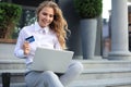 Online shopping concept. Young blonde woman holding a credit card and doing online payment with laptop outdoors Royalty Free Stock Photo