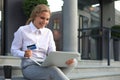 Online shopping concept. Young blonde woman holding a credit card and doing online payment with laptop outdoors Royalty Free Stock Photo