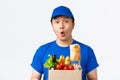 Online shopping, food delivery and shipment concept. Amazed and wondered asian male courier in blue uniform looking