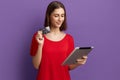 Online shopping. Happy young pretty brunette girl in red t-shirt holds tablet and showing a debit or credit card. Pays by internet Royalty Free Stock Photo