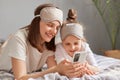 Online shopping. Internet browsing. Attractive woman with daughter using cell phone on bed at home watching video or checking Royalty Free Stock Photo