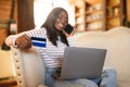 Online shopping. Millennial black lady with laptop using credit card, having phone call to order goods on web from home Royalty Free Stock Photo