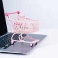 Online shopping. Mini empty pink shop cart trolley over a laptop computer on white table background, buying at home concept, close Royalty Free Stock Photo