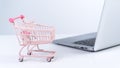 Online shopping. Mini empty pink shop cart trolley over a laptop computer on white table background, buying at home concept, close Royalty Free Stock Photo