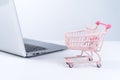 Online shopping. Mini empty pink shop cart trolley over a laptop computer on white table background, buying at home concept, close Royalty Free Stock Photo