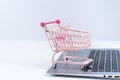 Online shopping. Mini empty pink shop cart trolley over a laptop computer on white table background, buying at home concept, close Royalty Free Stock Photo