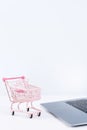 Online shopping. Mini empty pink shop cart trolley over a laptop computer on white table background, buying at home concept, close Royalty Free Stock Photo