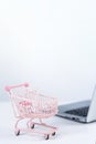 Online shopping. Mini empty pink shop cart trolley over a laptop computer on white table background, buying at home concept, close Royalty Free Stock Photo