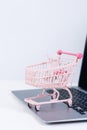 Online shopping. Mini empty pink shop cart trolley over a laptop computer on white table background, buying at home concept, close Royalty Free Stock Photo