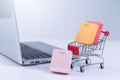 Online shopping. Mini shop cart trolley with colorful paper bags over a laptop computer on white table background, buying at home Royalty Free Stock Photo