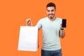 Online shopping. Portrait of happy buyer, brunette man holding shopping bags and cellphone. isolated on orange background