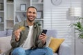 Online shopping. Portrait of a young African American man is sitting on the couch at home, holding a credit card and a Royalty Free Stock Photo