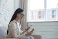 Online shopping. Satisfied young beautiful woman in glasses sitting on sofa near window at home. Holds a credit card and Royalty Free Stock Photo