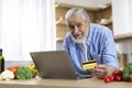 Online Shopping. Smiling Elderly Man Using Laptop And Credit Card In Kitchen Royalty Free Stock Photo