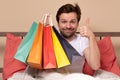Young man sitting at hte bed at home holding some shopping bags Royalty Free Stock Photo