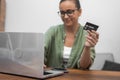 online shopping: A woman in glasses manages her credit card payment near her laptop.