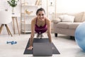 Online sports tutorials. Cheerful Latin girl doing plank exercise near laptop at home