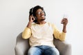 Online Streaming Services. Cheerful Black Guy Sitting On Chair And Listening Music Royalty Free Stock Photo