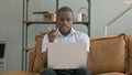 Online Video Chat on Laptop by African Man Sitting on Sofa Royalty Free Stock Photo