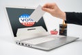 Online voting concept with a man with a ballot in hand putting a ballot toward the computer monitor