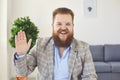 Online work video call home. A fat man with a beard greets with a hand in the camera online using a webcam video chat Royalty Free Stock Photo