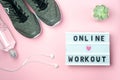 Online Workout - text on display lightbox on pink background. Flat lay - Sneakers, a bottle of water, white headphones. Sport