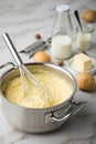 Ooking pot with mashed potatoes and ingredients as potato, milk, salt, butter, nutmeg with whisker and grinder on light marble