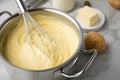 Ooking pot with mashed potatoes and ingredients as potato, milk, salt, butter, nutmeg with whisker and grinder on light marble