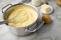 Ooking pot with mashed potatoes and ingredients as potato, milk, salt, butter, nutmeg with whisker and grinder on light marble