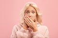 Oops. Portrait of shocked lady covering her mouth with both hands and staring at camera, pink studio background