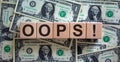 Oops sign on wooden cubes. Beautiful background from dollar bills, copy space. Concept