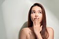 Oops! Surprised young Asian woman covering mouth with hands and staring at camera while standing against grey background