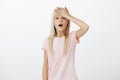 Oops, totally forgot to make homework. Studio shot of adorable worrying european young girl in pink t-shirt, holding