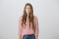 Oops, what have I done. Studio shot of worried beautiful young girl with blonde hair in striped shirt biting lower lip Royalty Free Stock Photo