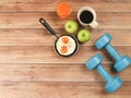 Op view of fried eggs in pan , orange juice , apples , black coffee and blue dumbbells on wooden background Royalty Free Stock Photo