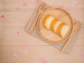 Op view vanilla cake roll on wooden dish with wooden spoon,fork,pink flower petals on wooden background