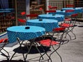 Open-air bistro modest setting with folding chairs, tables with ashtrays on sunny terrace