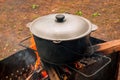 Open air kitchen at party picnic. Pilaf cooking on fire outdoor. Big pot closed with cover stays on wire rack and steams. Close up