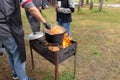 Open air kitchen at party picnic. Pilaf cooking on fire outdoor. Chef cook is stirring meal dish in big pot by ladle. Bushpot