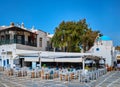 Colorful outdoor cafe or restaurant in typical Greek island town. Greek Orthodox church, blue dome, tourists roam around