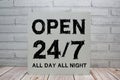 Open 24 7 All Day All Night sign with blackboard on white brick background Royalty Free Stock Photo