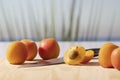 An open apricot next to a knife, surrounded by whole apricots on a cutting board