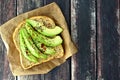 Open avocado sandwich on paper against rustic wood